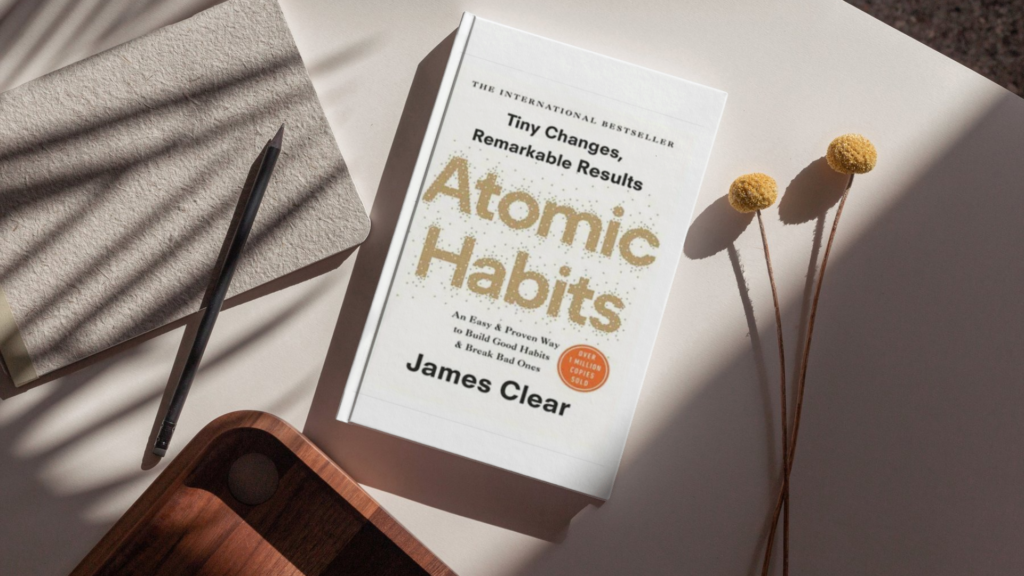 Minimalist Atomic Habits by James Clear flat lay with notebook, pencil, and soft shadows — aesthetic feature image for a self-help book review about habit building, productivity, consistency, and personal growth.